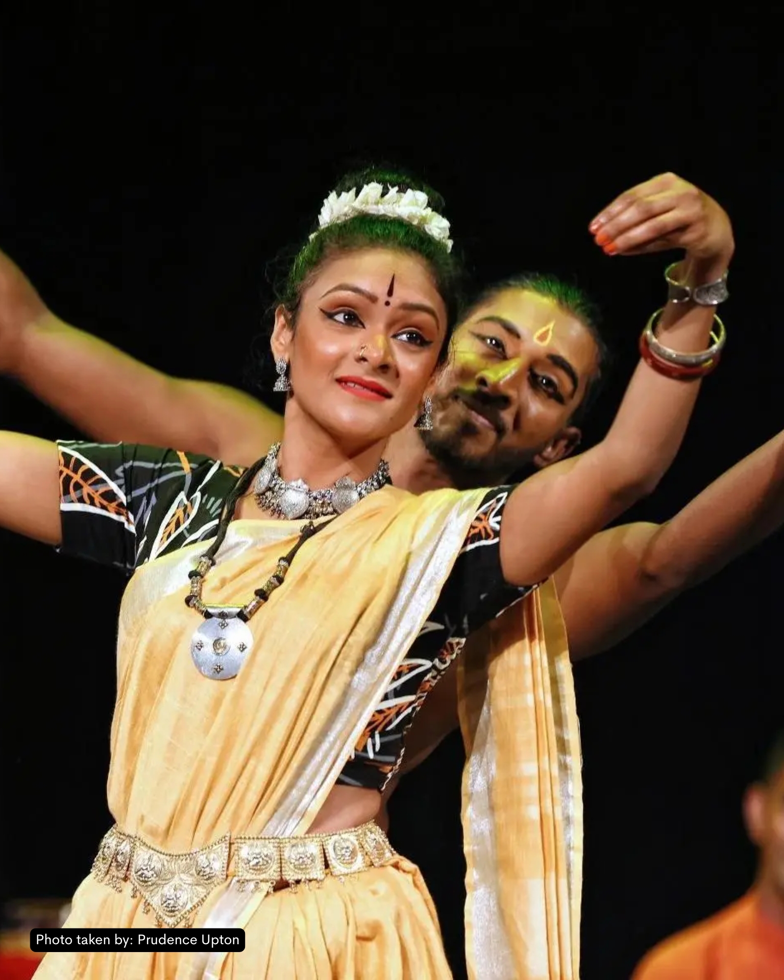 Archive photo from Bhoomi at the Sacred Music Festival 2019 — Kersh in Bharatanatyam mid-pose, set against a natural-toned backdrop, festival crowd visible at edge of frame.